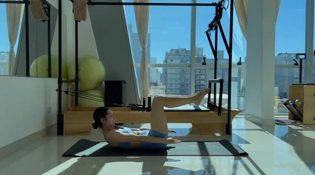 Alumna acostada en el mat con las piernas en alto realizando The Hundred, ejercicio de Pilates Mat