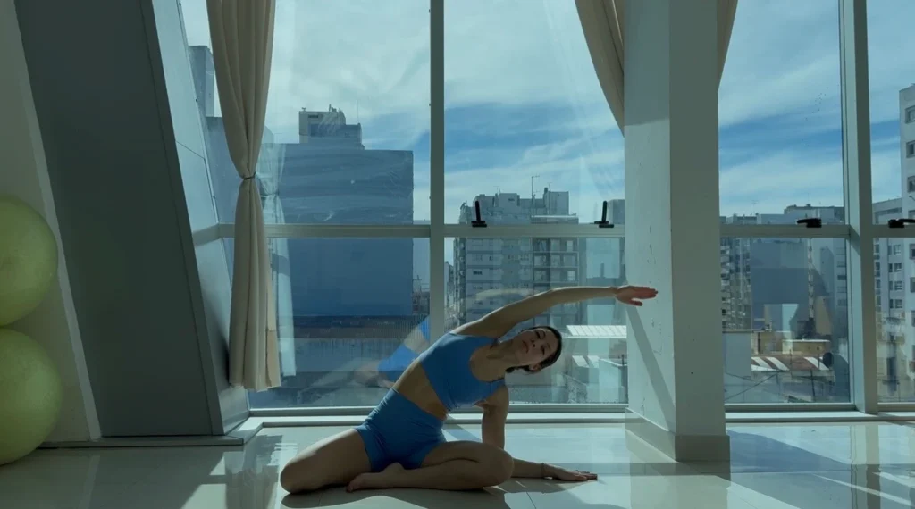 Alumna sentada en el mat haciendo un estiramiento lateral, movimiento de preparación de la clase de Pilates Mat